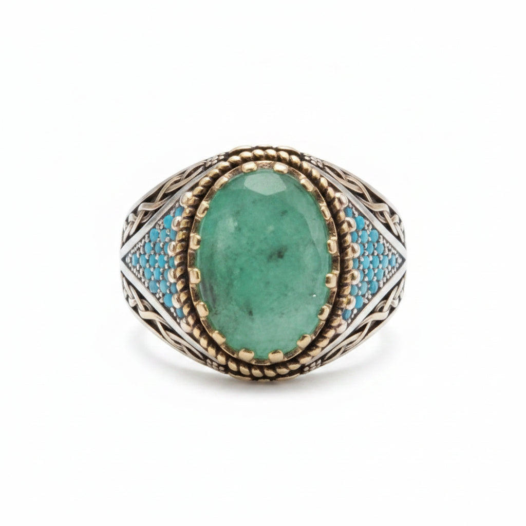 A teardrop-shaped ring featuring a green emerald-cut stone in a textured rose gold setting with light blue enamel accents, displayed on a beige jewelry box with price tags.