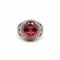 A silver-toned ring with a large faceted dark red gemstone, displayed on a textured beige surface with a price tag partially visible.