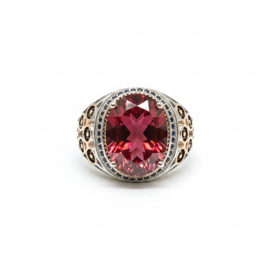 A silver-toned ring with a large faceted dark red gemstone, displayed on a textured beige surface with a price tag partially visible.
